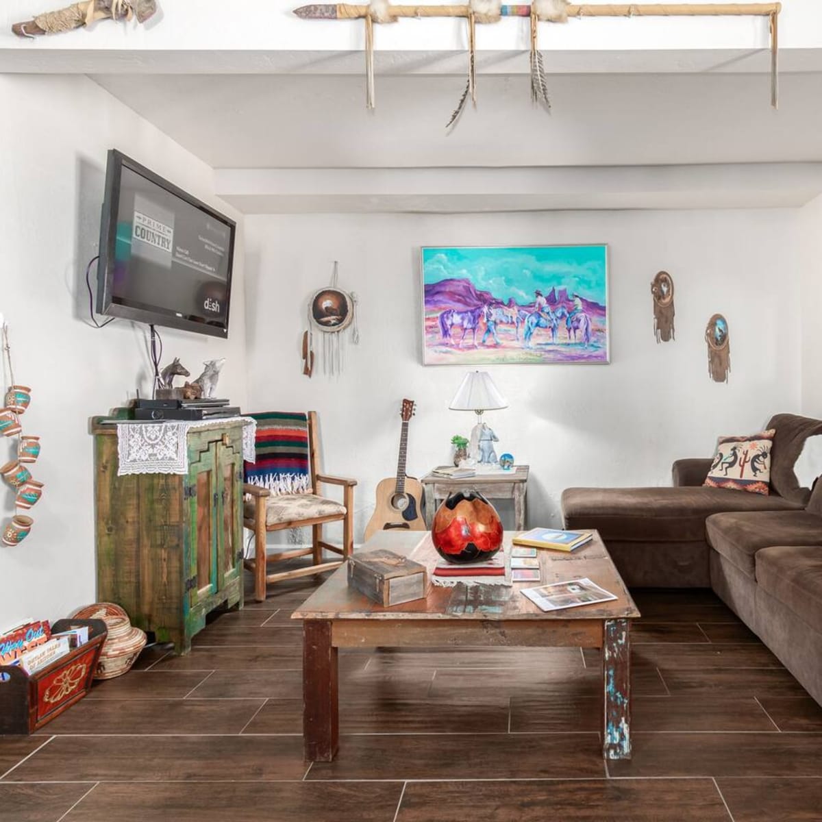 A living room with a brown couch, a wooden coffee table, a guitar, and various decorative items on the walls.