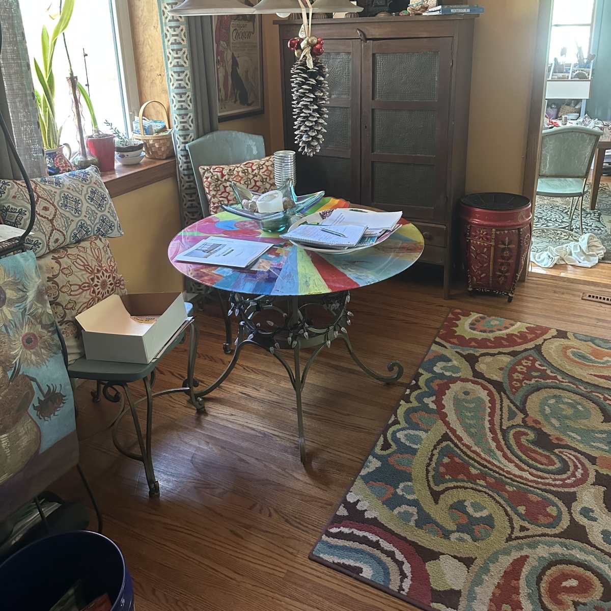 A cozy dining area featuring a colorful table, two chairs, a wooden cabinet, and a patterned rug.