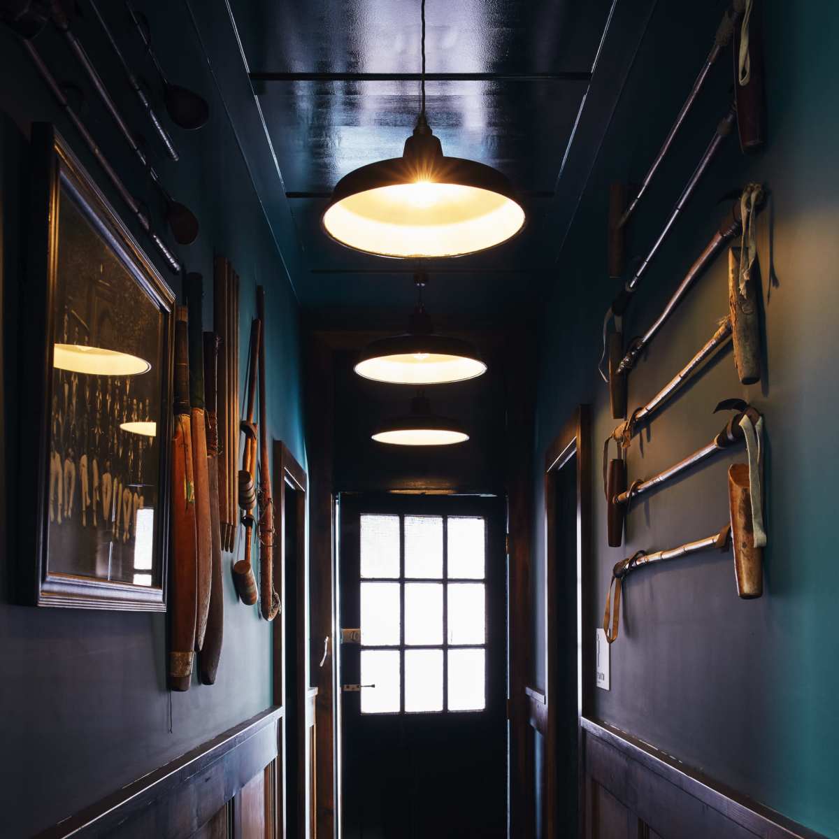 A narrow hallway features several illuminated pendant lights and walls adorned with various vintage tools and paddles.