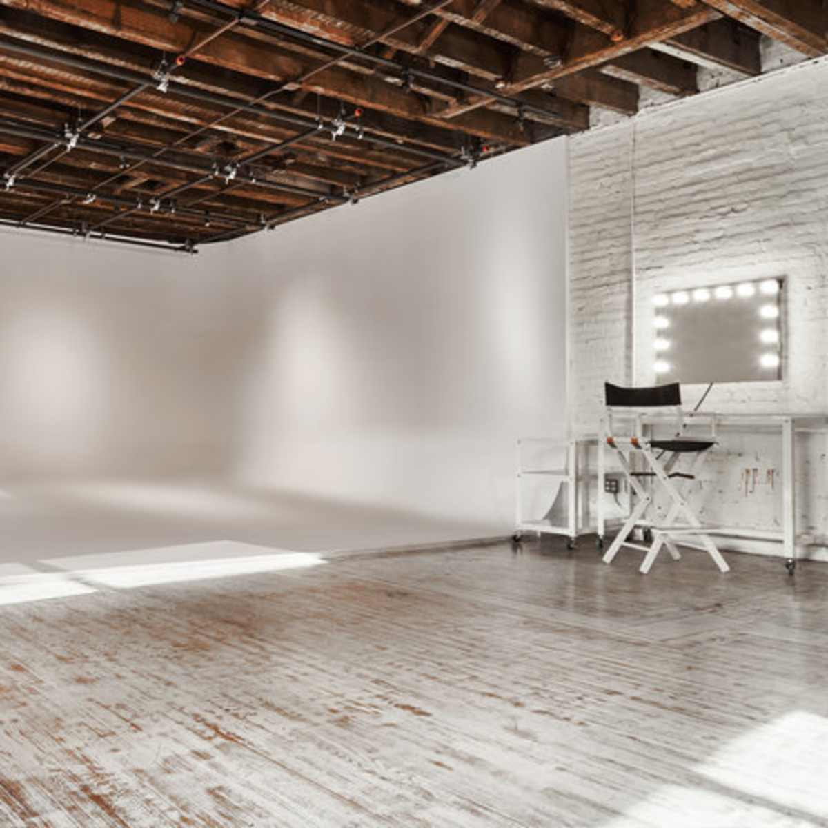 A spacious, well-lit studio with a white backdrop, hardwood floors, and a vanity mirror with lights.