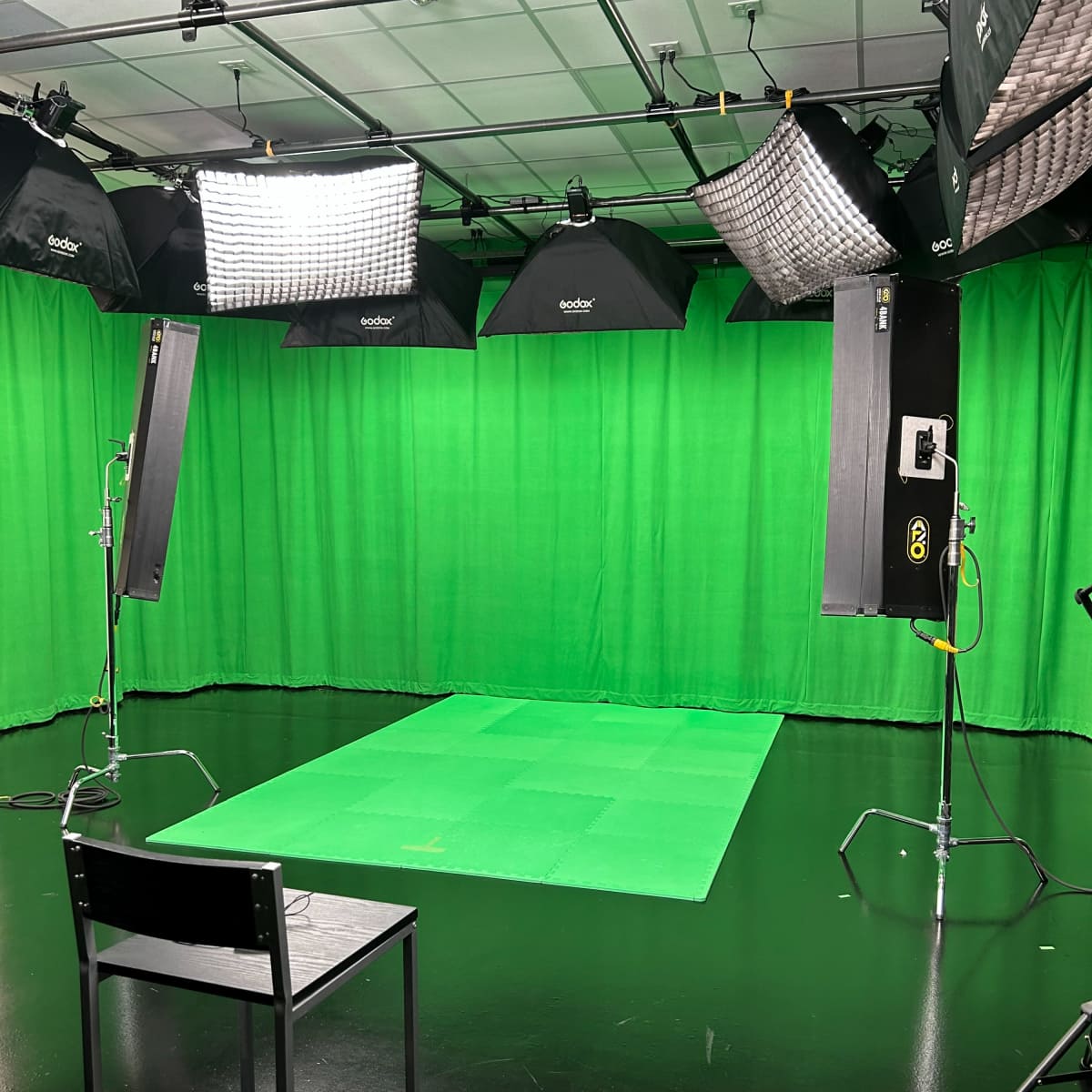 A green screen studio setup, featuring softbox lights and a green backdrop along with a black chair positioned in front.