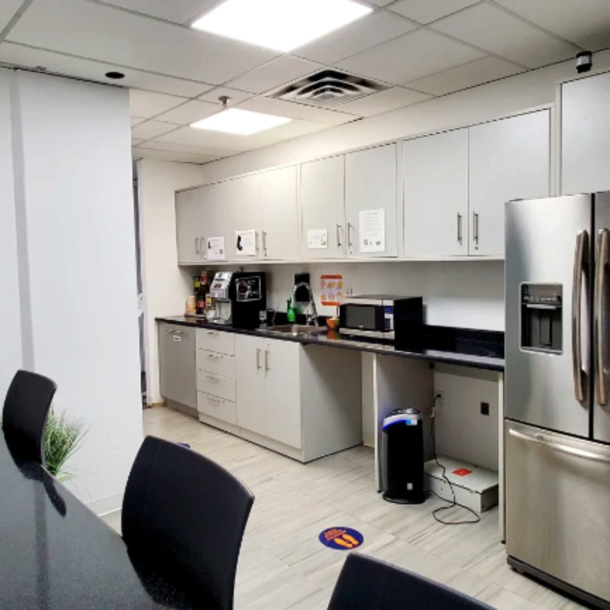 A modern kitchen area with gray cabinets, a stainless steel refrigerator, and a countertop equipped with appliances like a microwave and coffee maker.