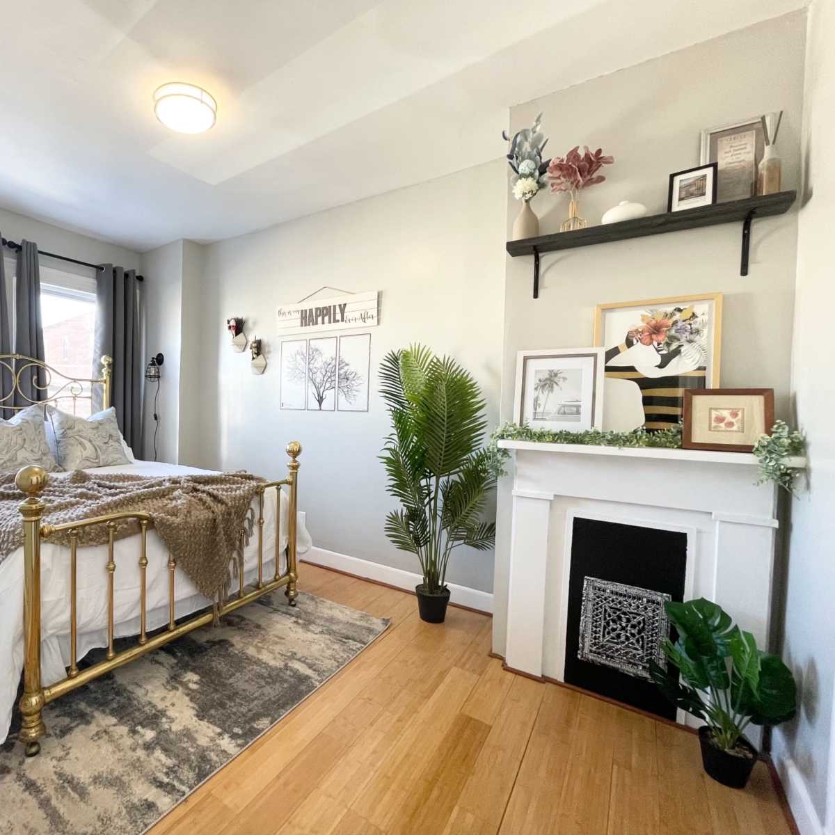 A well-decorated bedroom with a gold bed frame, a patterned rug, and a decorative fireplace, complemented by plants and wall art.