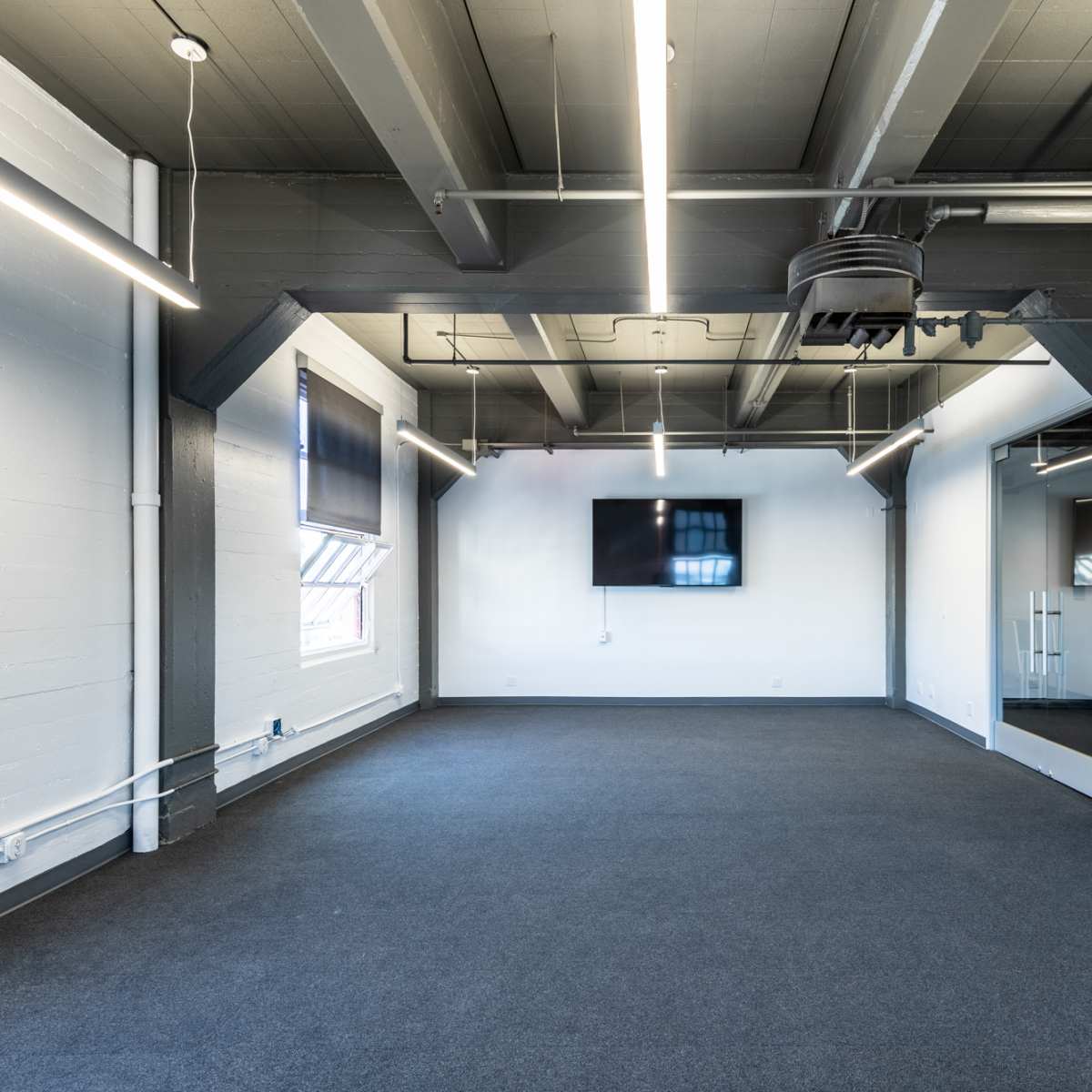 A spacious, empty room with gray walls, large windows, and modern lighting fixtures.