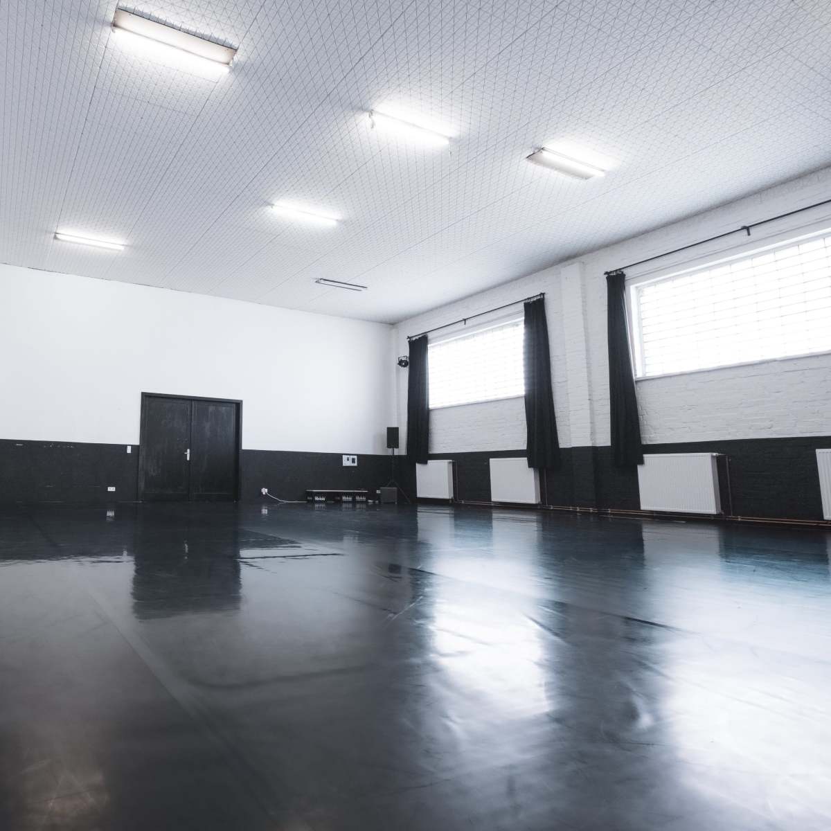 A spacious indoor room with black and white walls, fluorescent lighting, and a shiny floor.