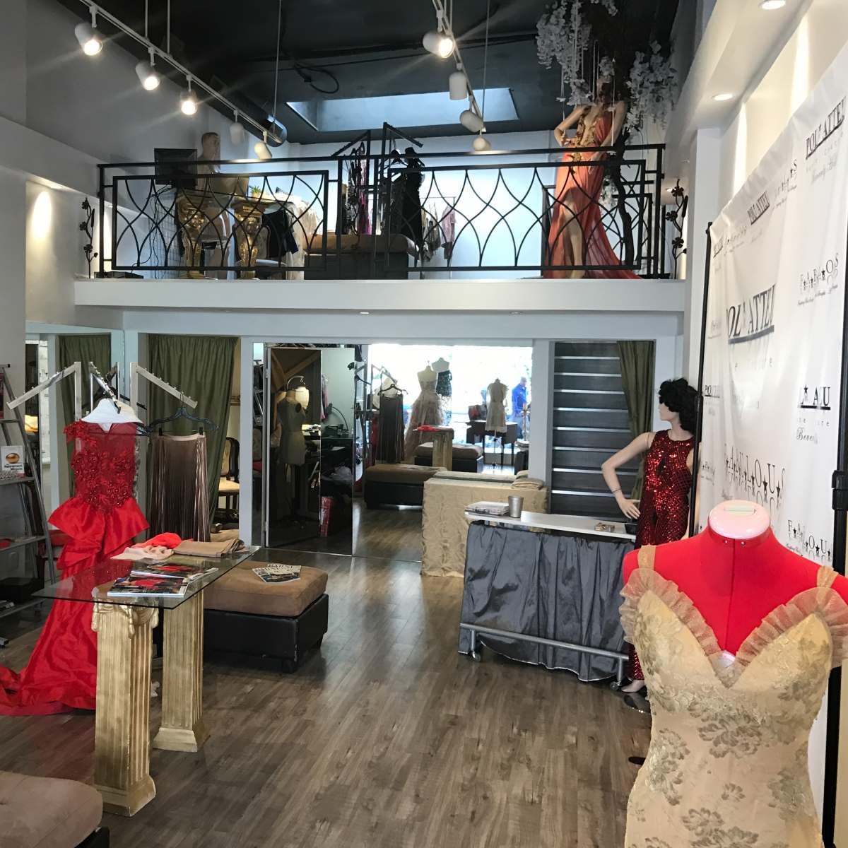 A spacious boutique with a variety of dresses displayed on racks, a staircase leading to a second level, and a fitting area visible in the background.