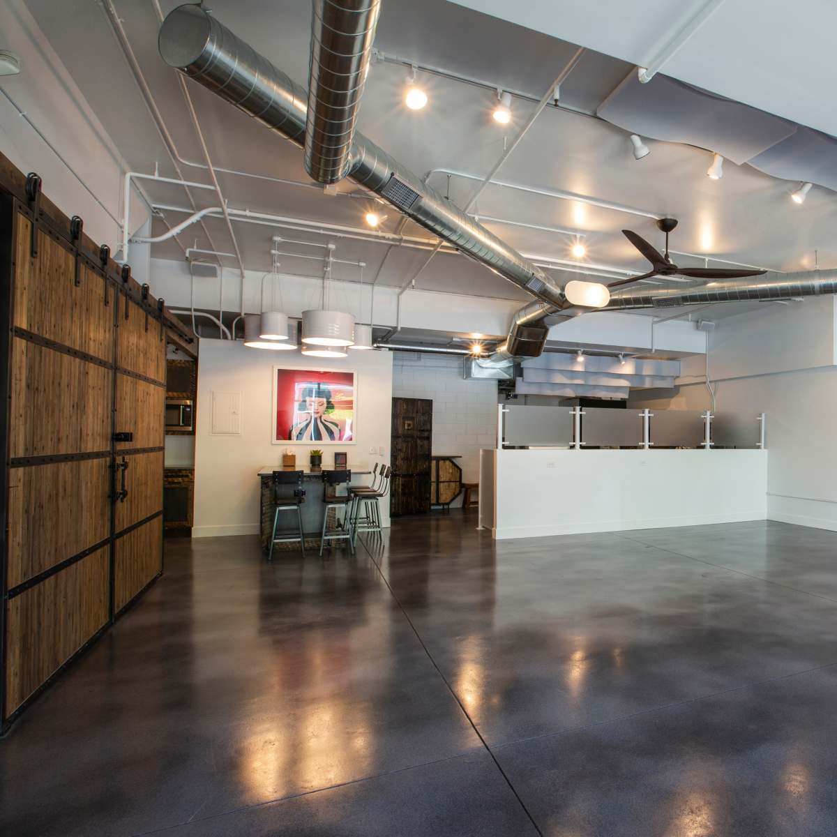 An open, modern interior space with polished concrete floors, exposed ductwork, and a large sliding wooden door.
