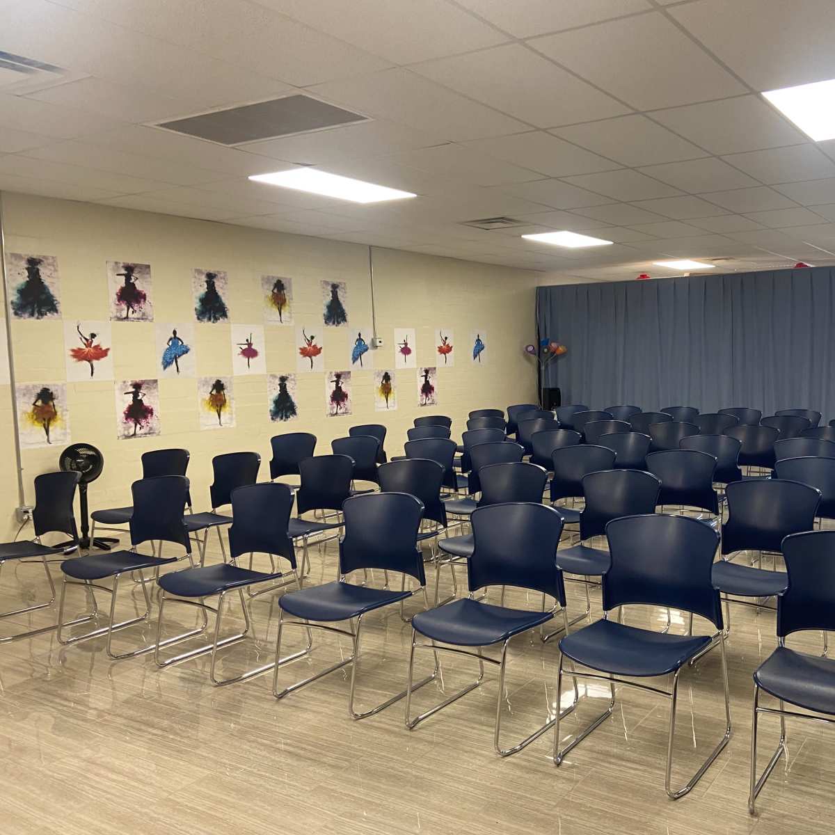 A rows of navy blue plastic chairs arranged in a large, well-lit room with artwork displayed on the walls.