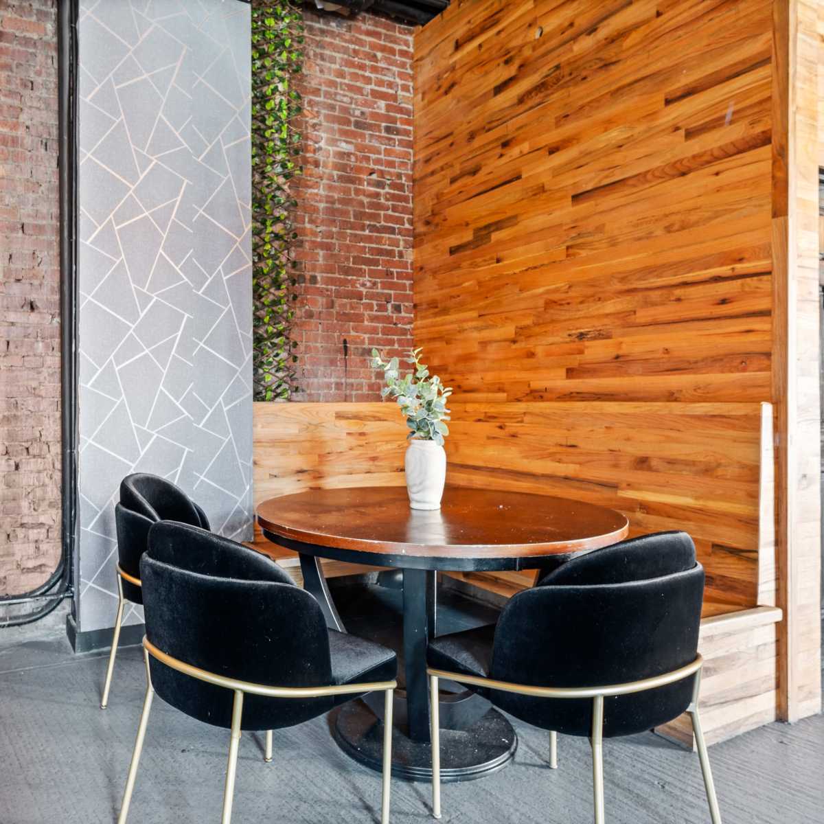 A small dining area features a round black table with four black chairs against a backdrop of exposed brick and wooden walls.