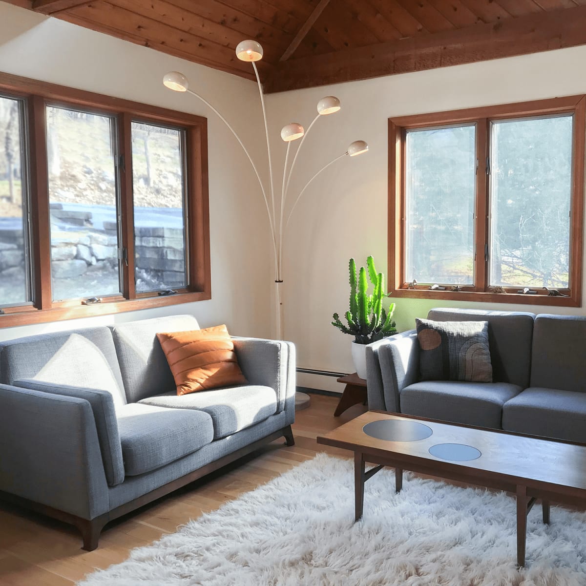 A living room with a gray sofa, a gray loveseat, a wooden coffee table, and a floor lamp, all complemented by natural light coming through large windows.
