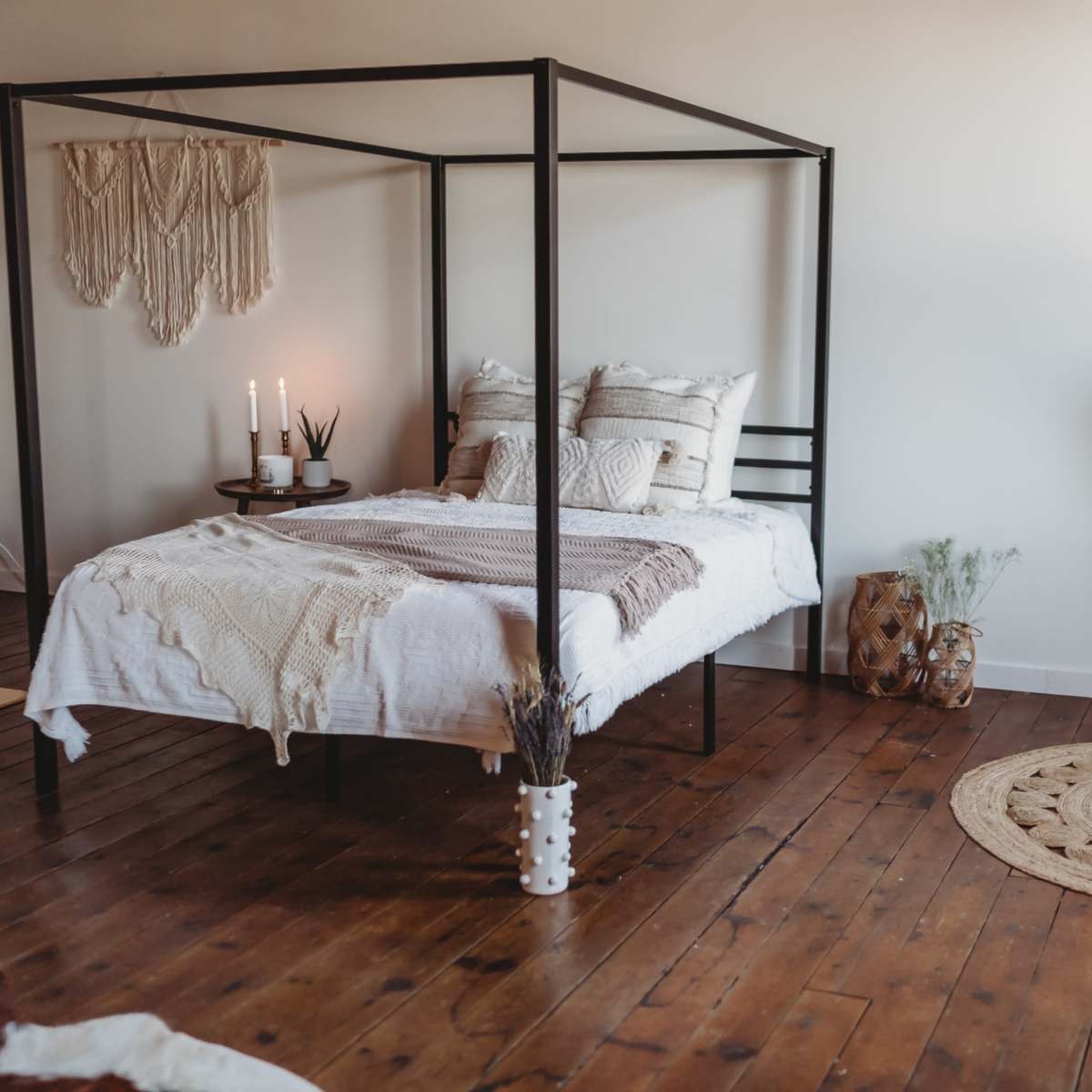 A four-poster bed with a white comforter is centered in a cozy room featuring wooden floors and a large mirror.