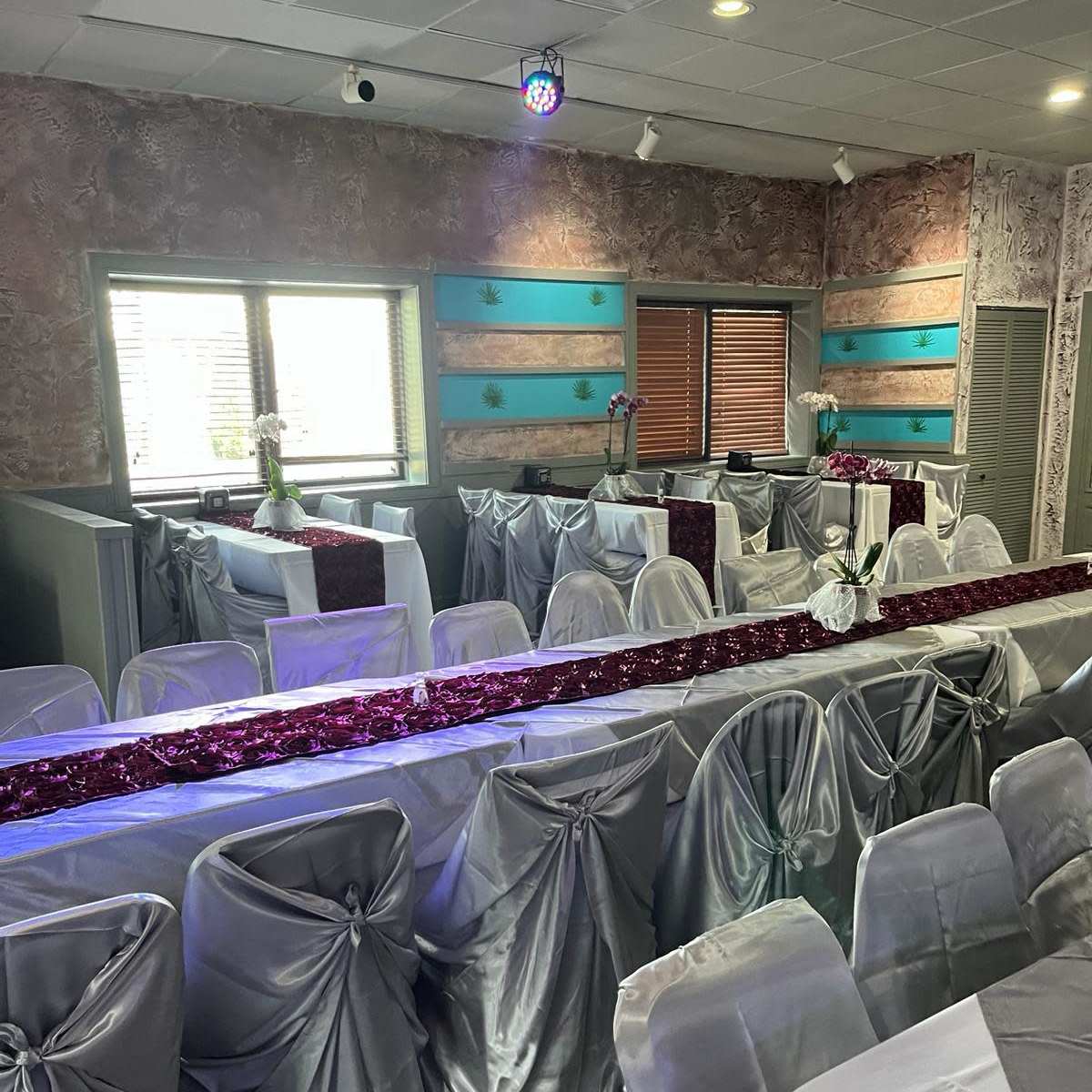 A banquet room is arranged with silver tablecloths and a decorative red runner, featuring tables set for an event under a disco ball.