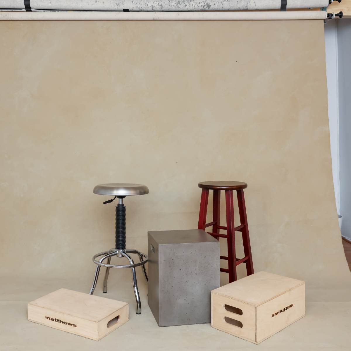 A plain backdrop with two wooden stools and a concrete block arranged on the floor.