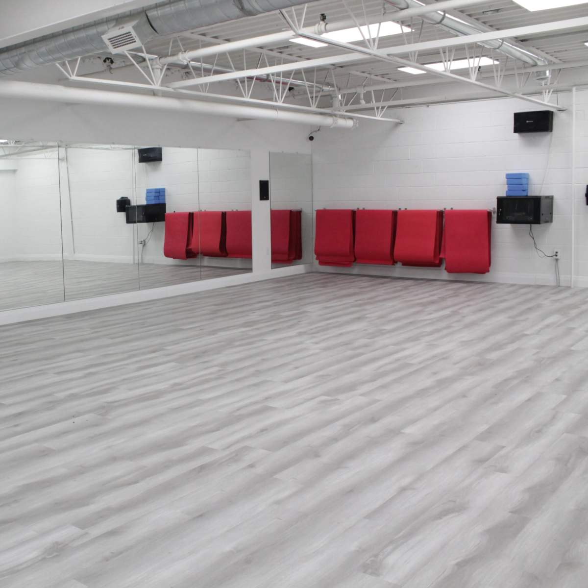 An empty, well-lit room with gray laminate flooring, white walls, a large mirrored wall, and red wall-mounted benches.