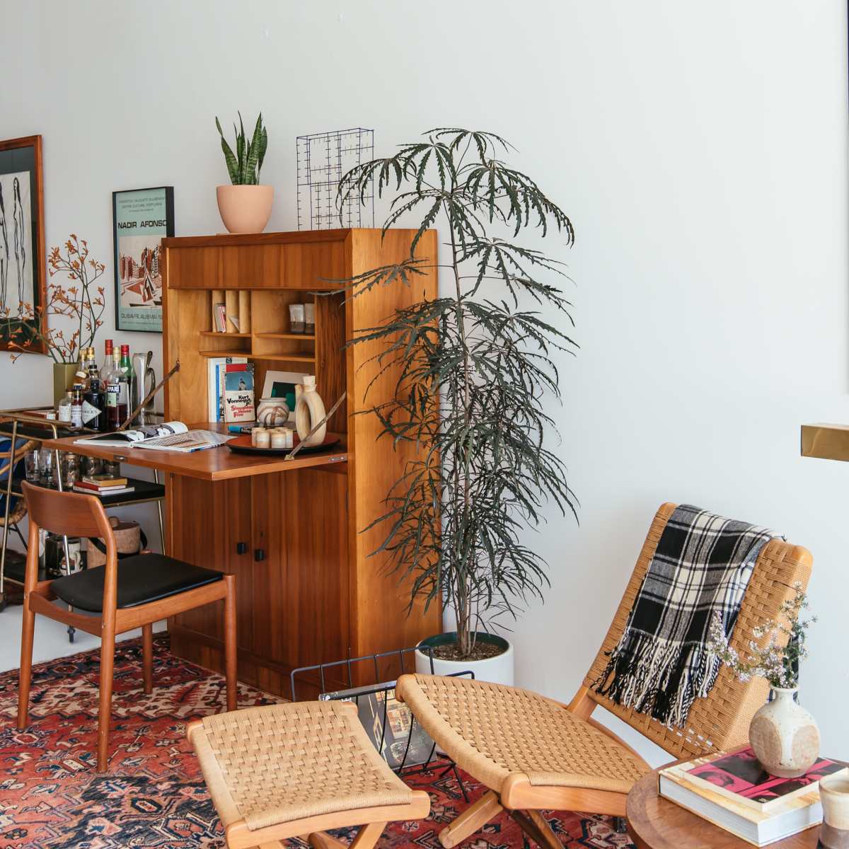 A well-furnished living room corner with a wooden desk, a modern poster on the wall, a potted plant, and a cozy seating area.