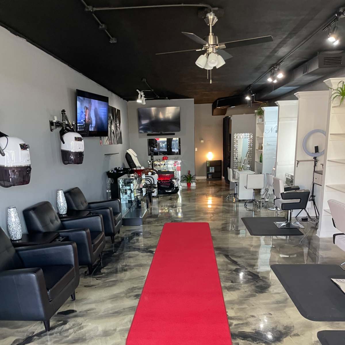 A beauty salon interior featuring a red carpet, black leather chairs, and sleek furnishings under a modern lighting setup.
