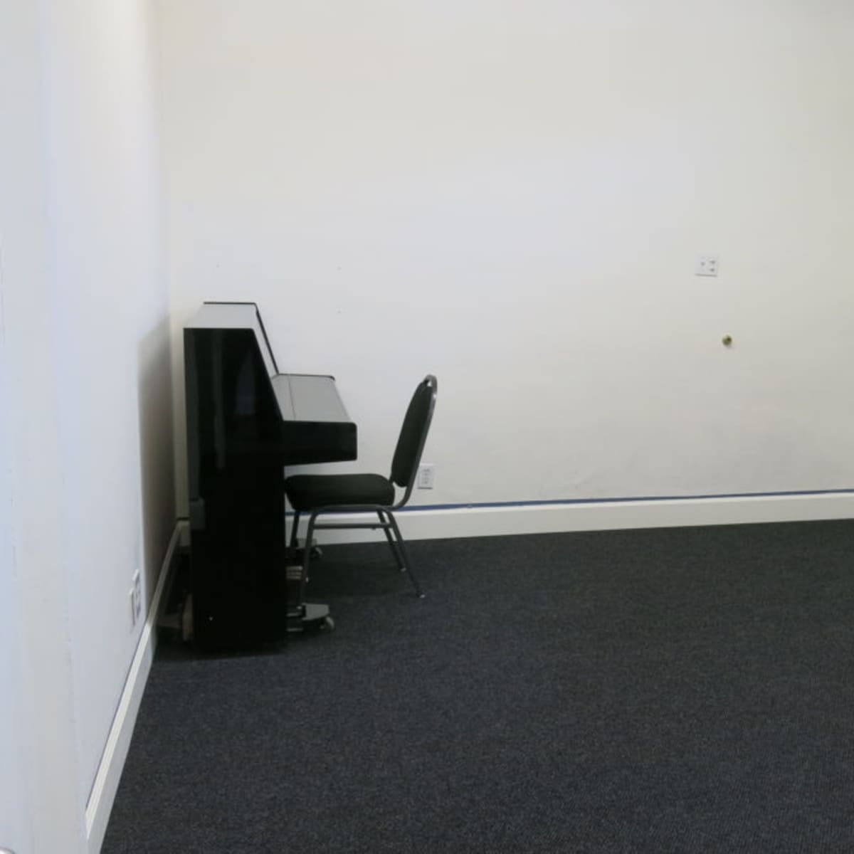 A sparsely furnished room with a piano, a chair, and a whiteboard near a door.