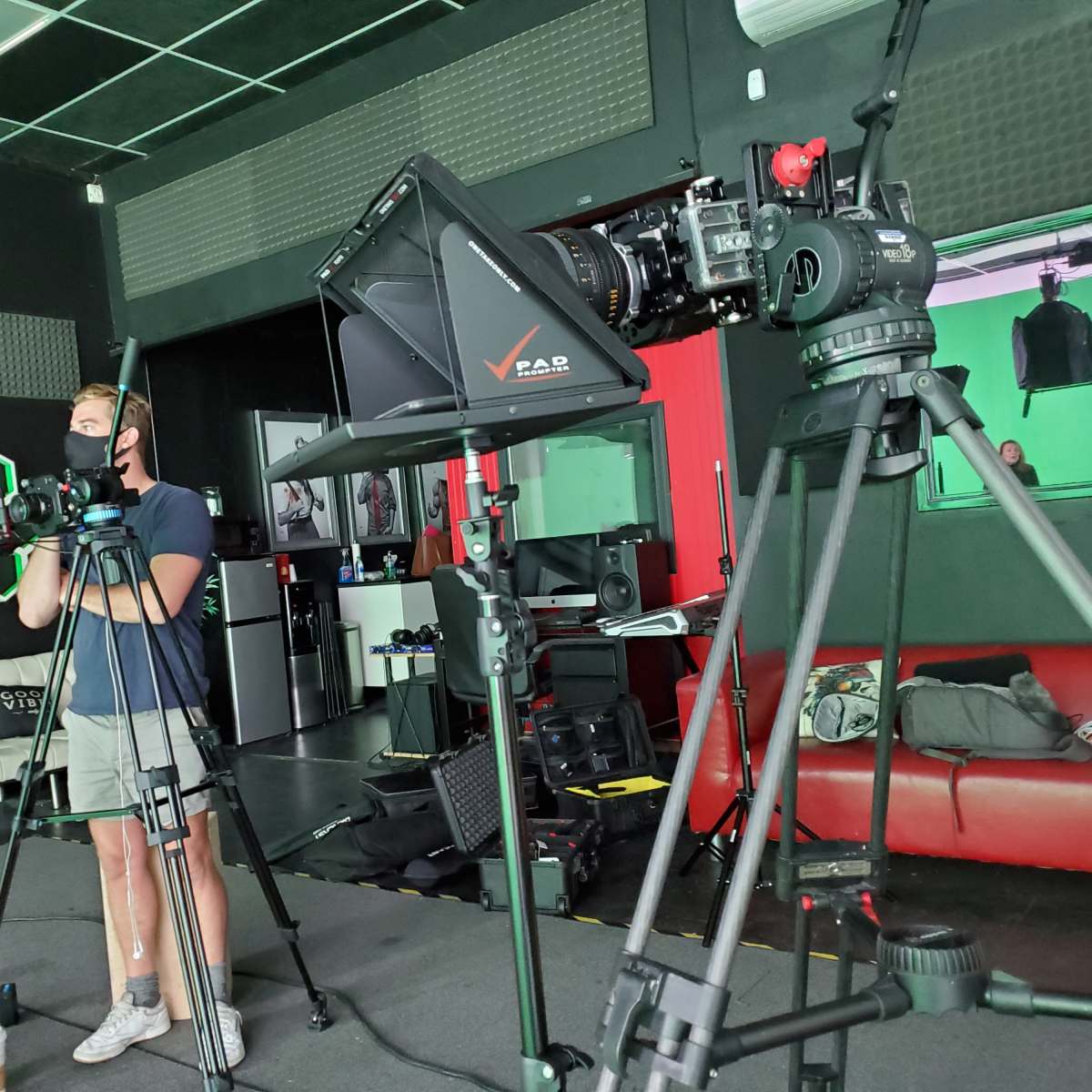 A photographer operates a camera on a tripod in a studio equipped with various filming equipment and a backdrop.