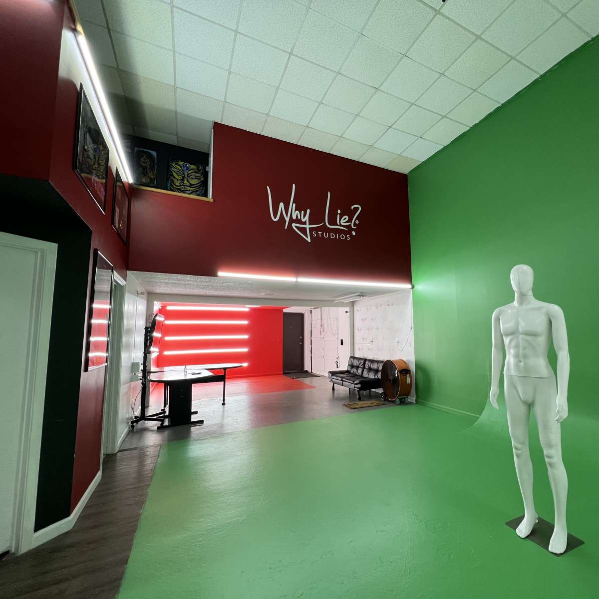The interior of a studio features a green wall, a white mannequin, and a red accent wall with the text "Why Lie? Studio" displayed prominently.