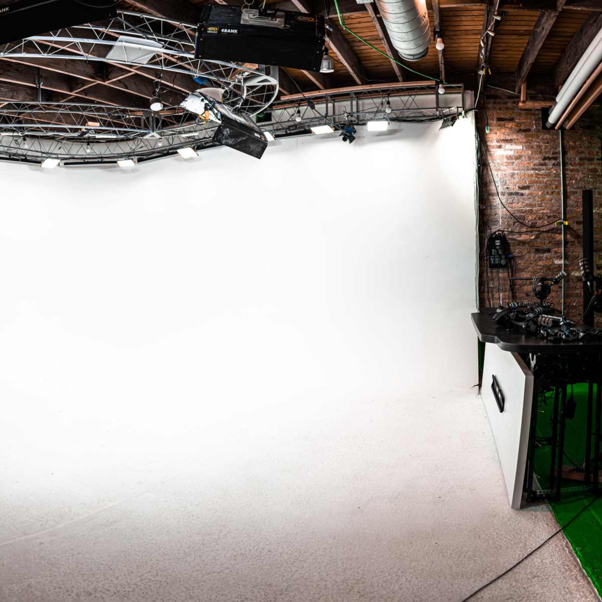 A spacious photography studio with a blank, white backdrop and overhead lighting fixtures.