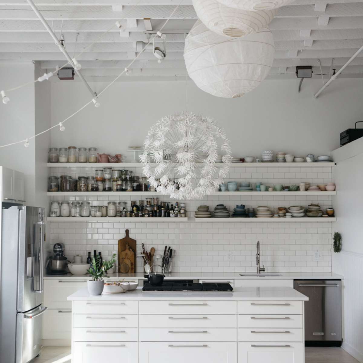 A modern kitchen features white cabinetry, open shelving with dishware, a central island with a cooktop, and pendant lighting.