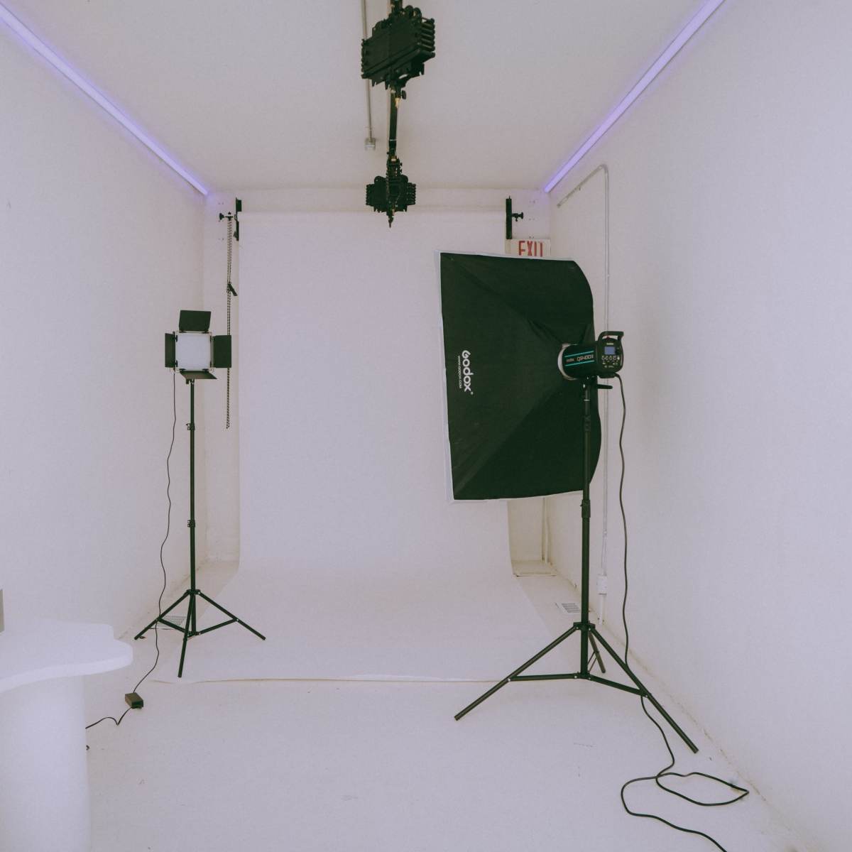 A minimalist photography studio with a plain white backdrop, softbox lighting, and a small table in the corner.