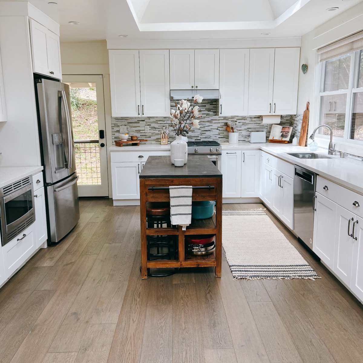 A modern kitchen with white cabinetry, stainless steel appliances, and a wooden island in the center.
