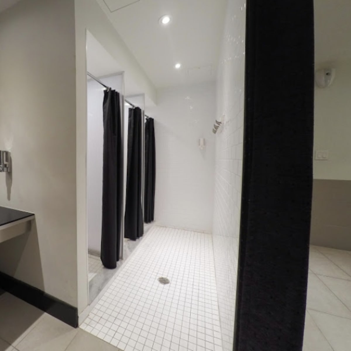 A bathroom with a changing area that includes a counter with lights and two separate shower stalls with dark curtains.