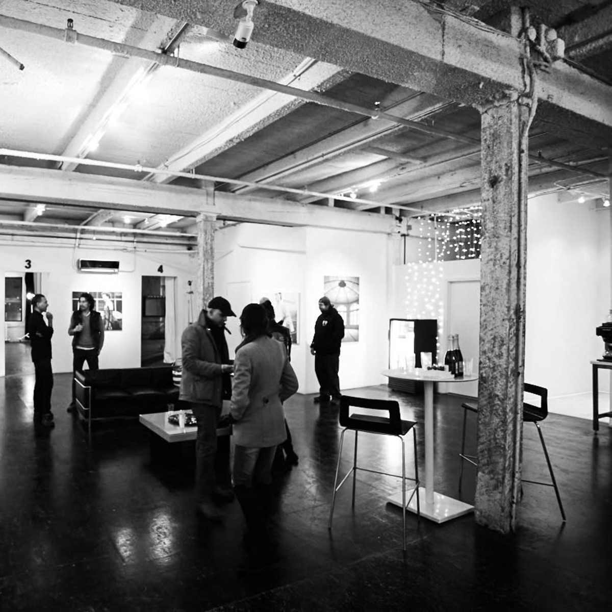 A group of people is exploring an art gallery featuring black and white photographs along the walls and a seating area in the center.