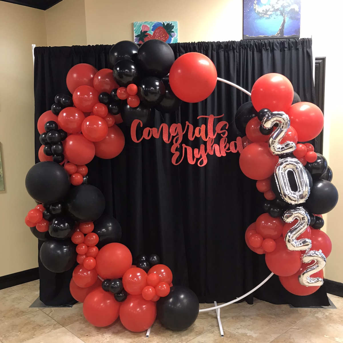 A decorative arch made of red, black, and silver balloons, with a "Congrats Erynka 2022" sign, set against a black backdrop.