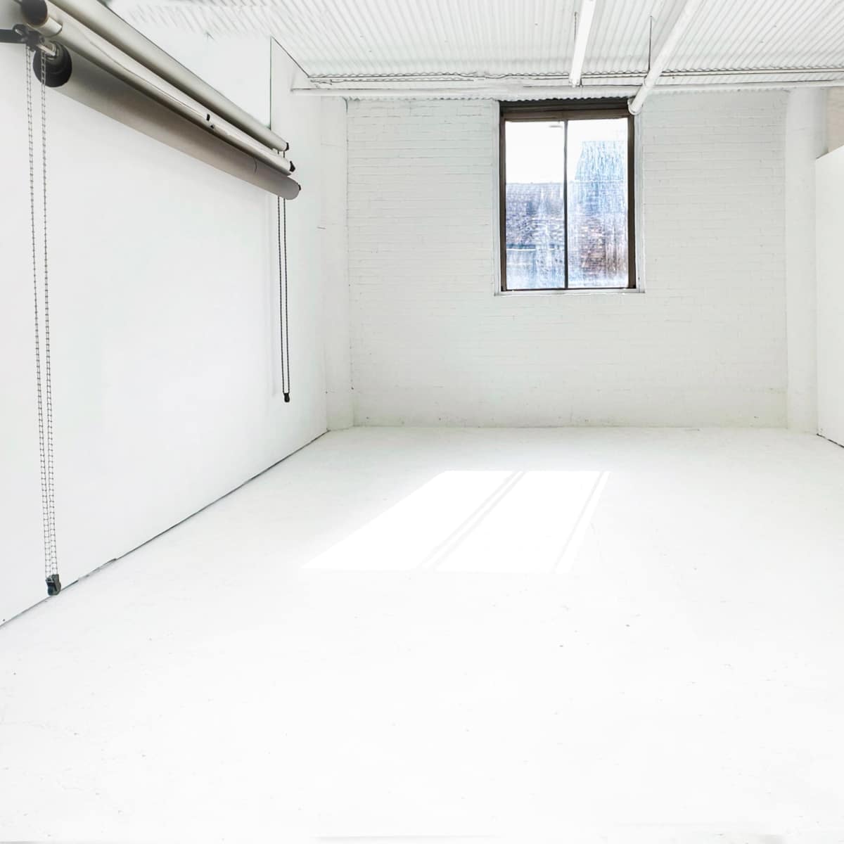 A bright, empty room with white walls and a window allowing natural light to enter.