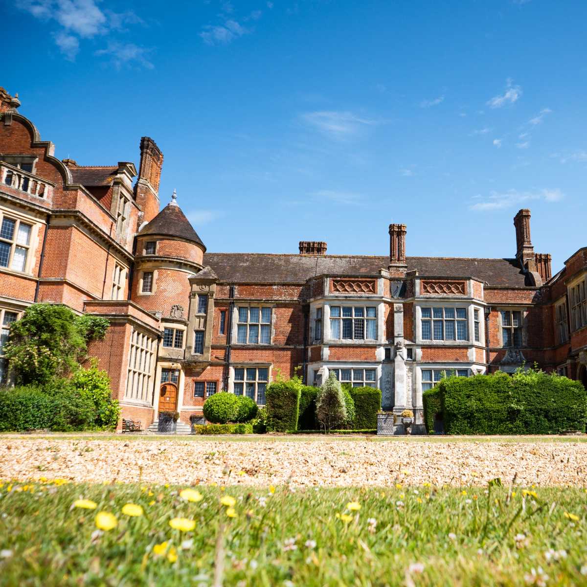 A large, historic brick mansion with a manicured lawn and a clear blue sky in the background.