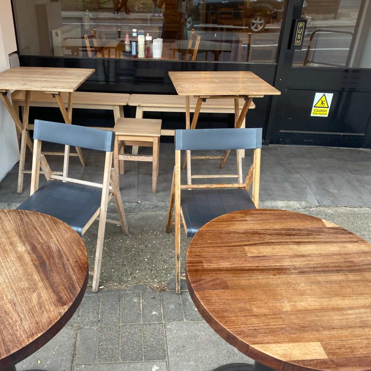 Several wooden tables and chairs arranged outside a café.