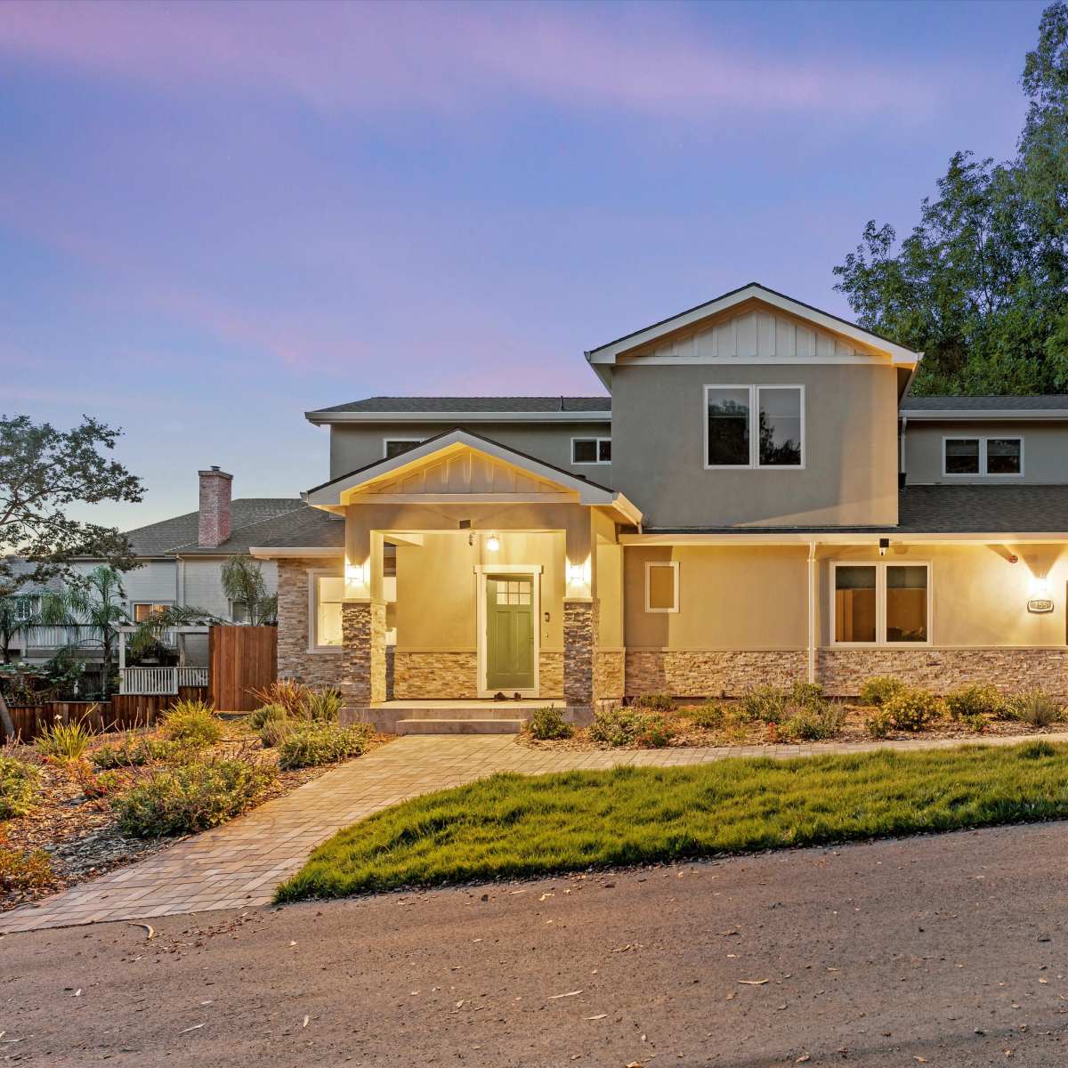A two-story house with a landscaped front yard and a driveway showcases a red car parked beside it during twilight.