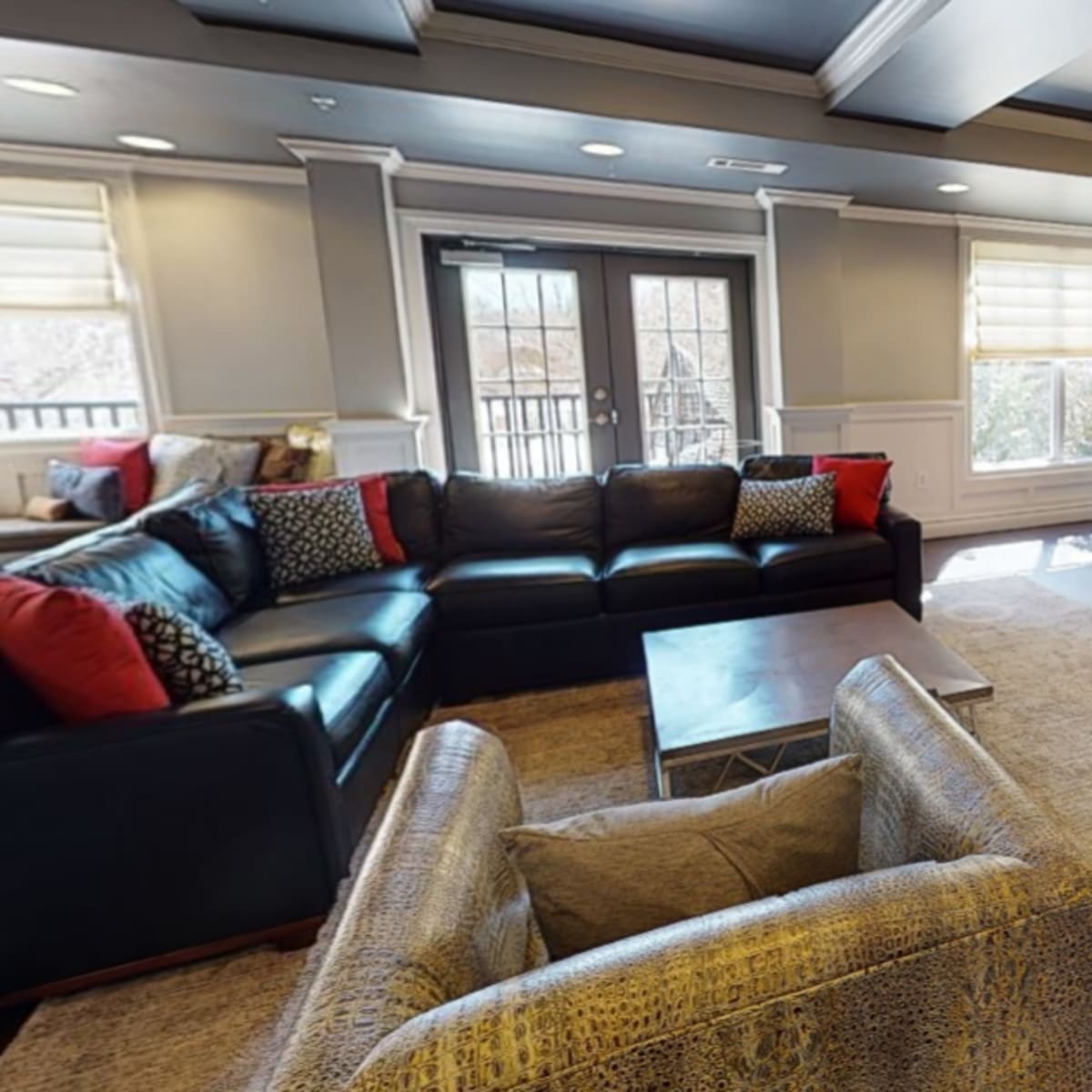 A modern living room with a black sectional sofa, a coffee table, and a fireplace, all surrounded by neutral-toned walls and large windows letting in natural light.