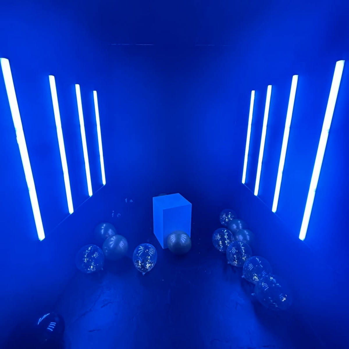 The scene features a dark room illuminated by vertical blue neon lights, with a solid blue cube at the center and several transparent spheres scattered on the floor.