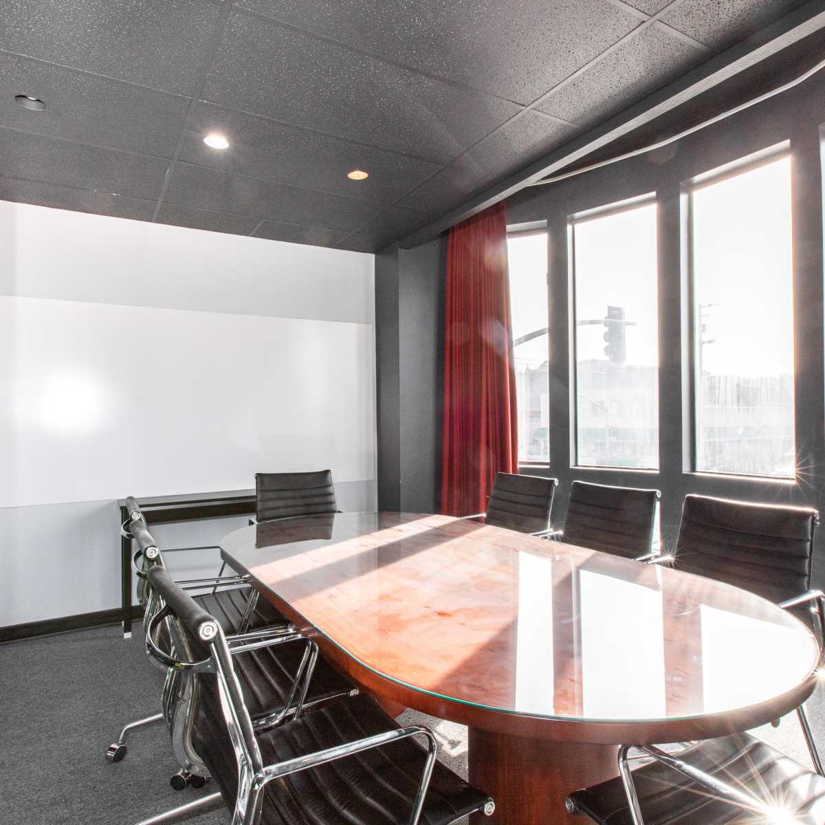 A modern conference room with a large oval table surrounded by black chairs and large windows allowing natural light.