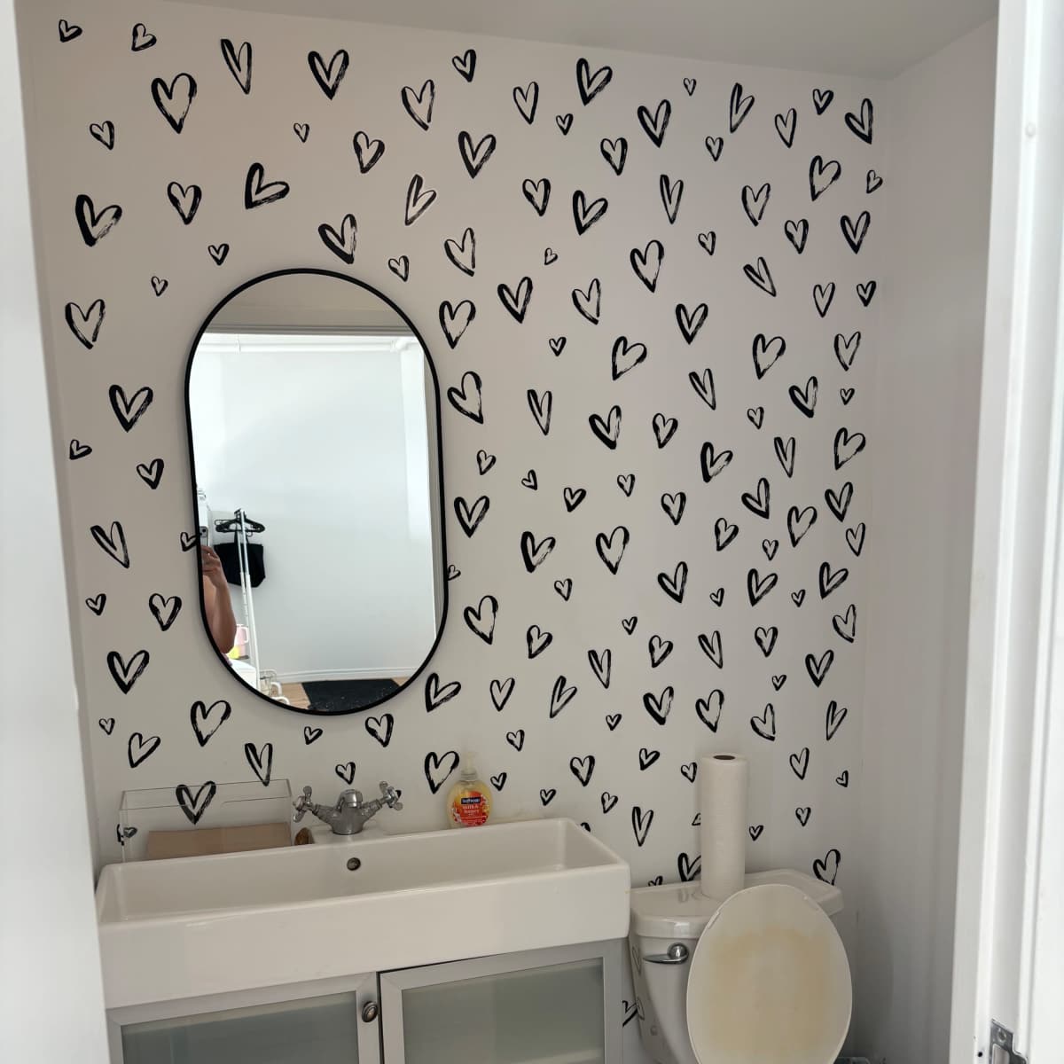 A small bathroom featuring a sink with a mirrored cabinet above it, a toilet, and walls decorated with black heart shapes.