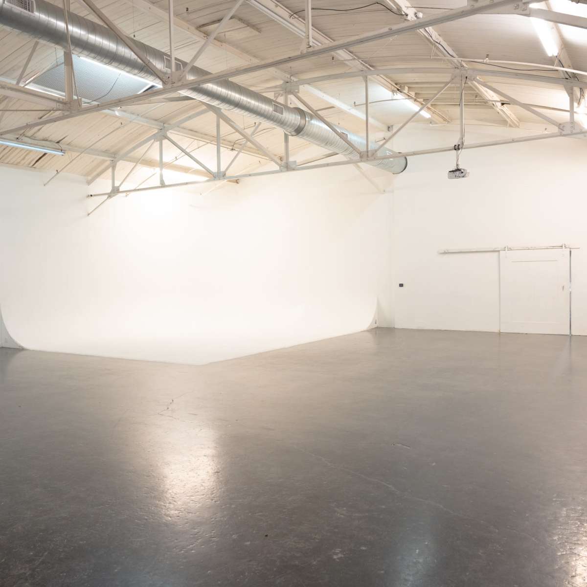 A spacious, empty studio with a smooth, white backdrop and polished concrete flooring.