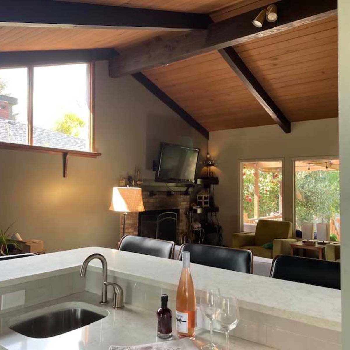 An open-concept living area with a kitchen bar, a stone fireplace, and large windows letting in natural light.
