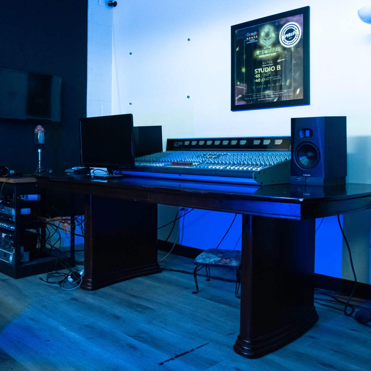 A music studio is equipped with a large mixing console, computer monitors, speakers, and a microphone on a polished wooden desk.