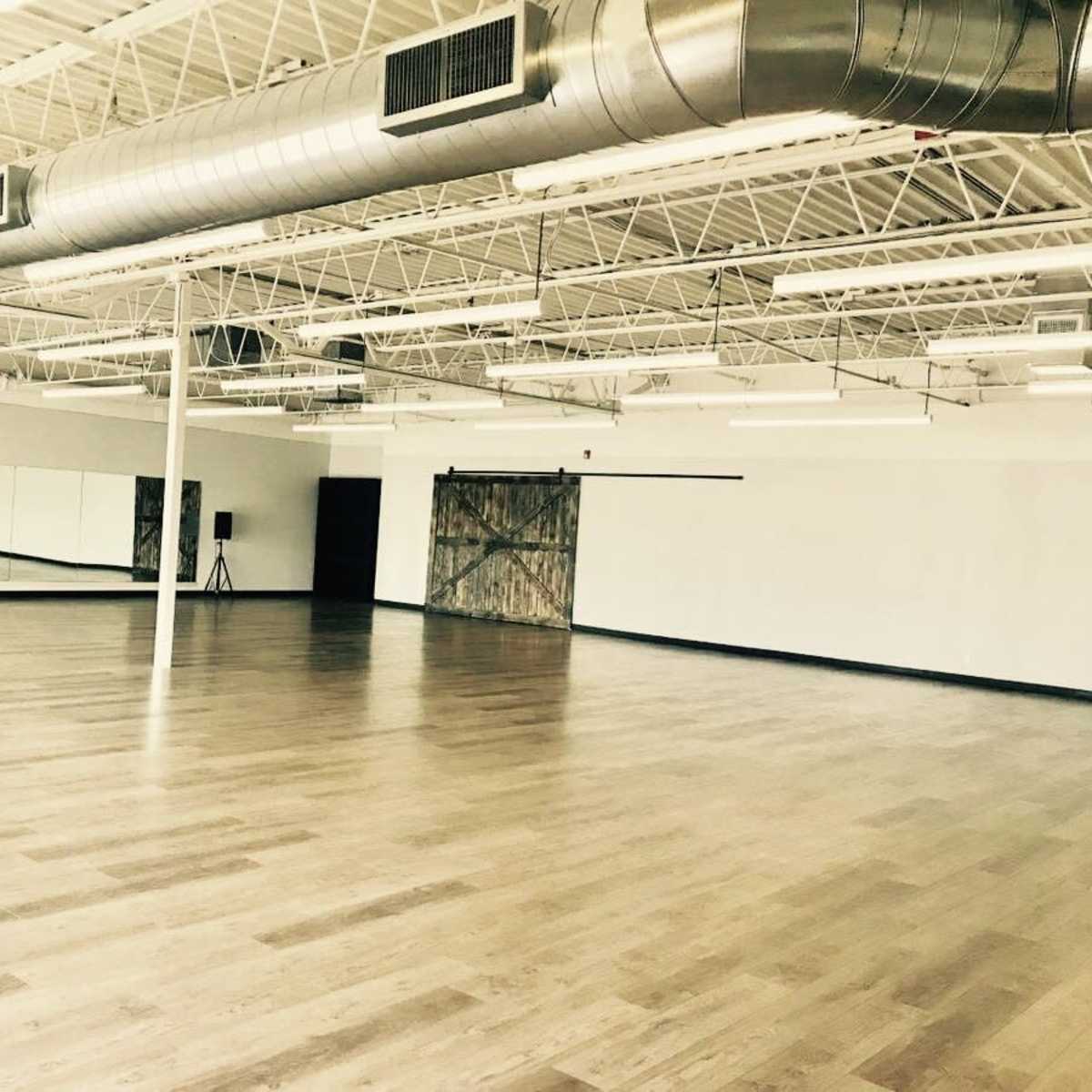 A spacious dance studio with wooden flooring, large mirrors, and industrial-style ventilation.