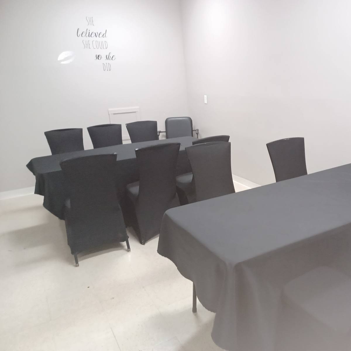 A room with several black-covered tables and chairs arranged neatly against light-colored walls.