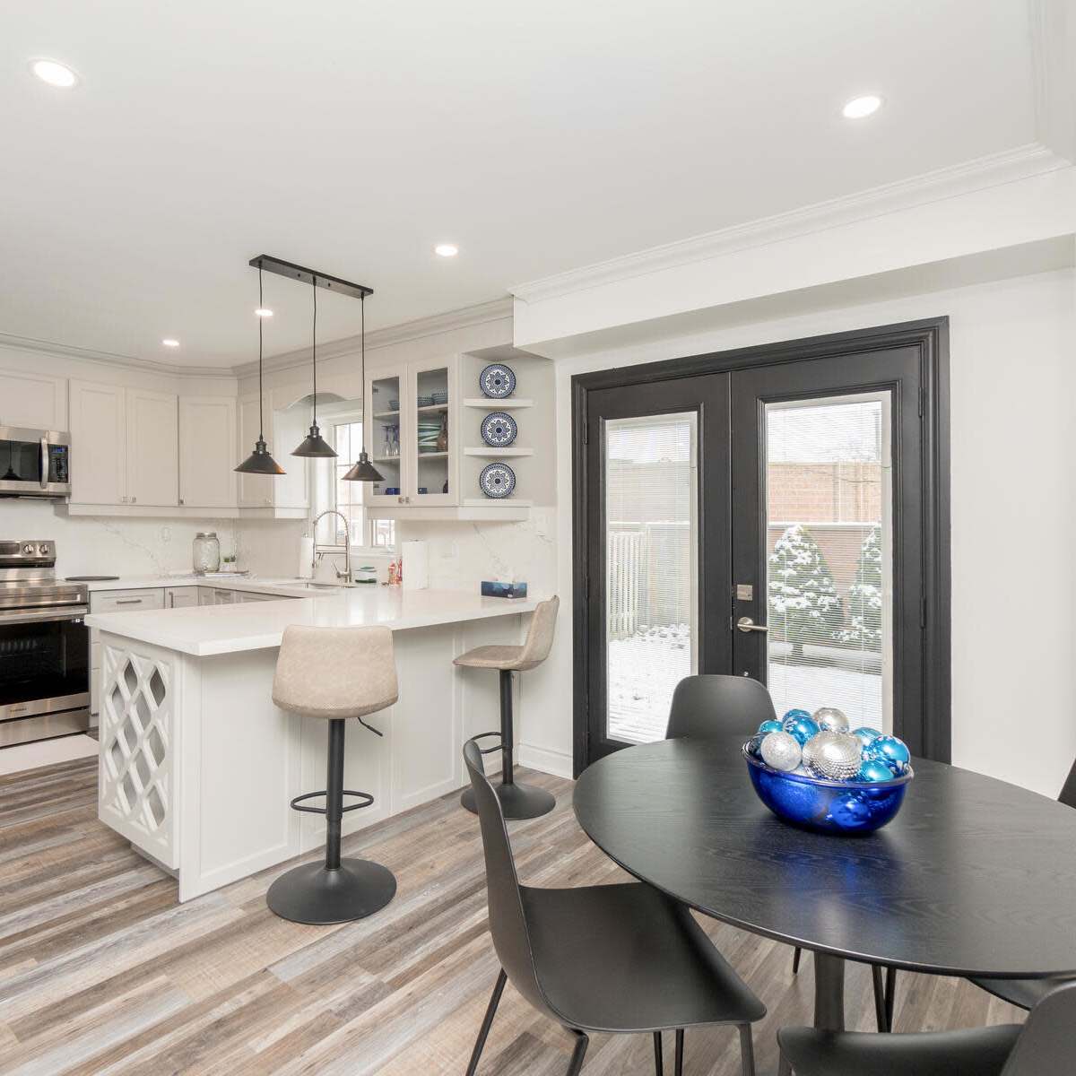 A modern kitchen with stainless steel appliances, a central island, and a dining area featuring a round table with a blue glass bowl.