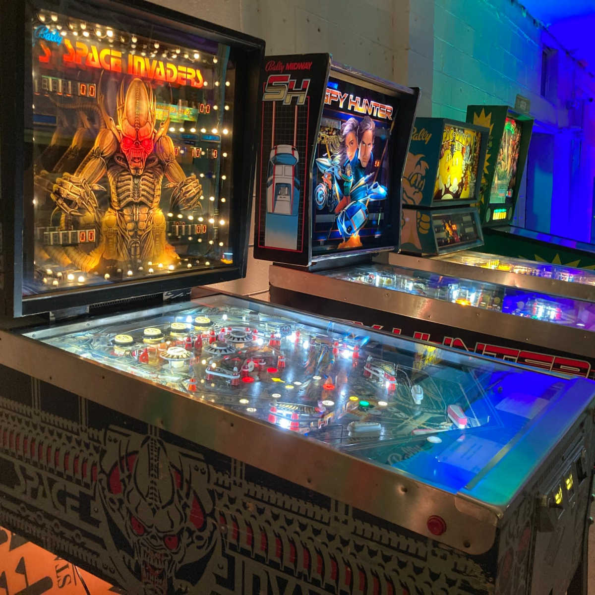 A row of vintage pinball machines in a brightly lit arcade.