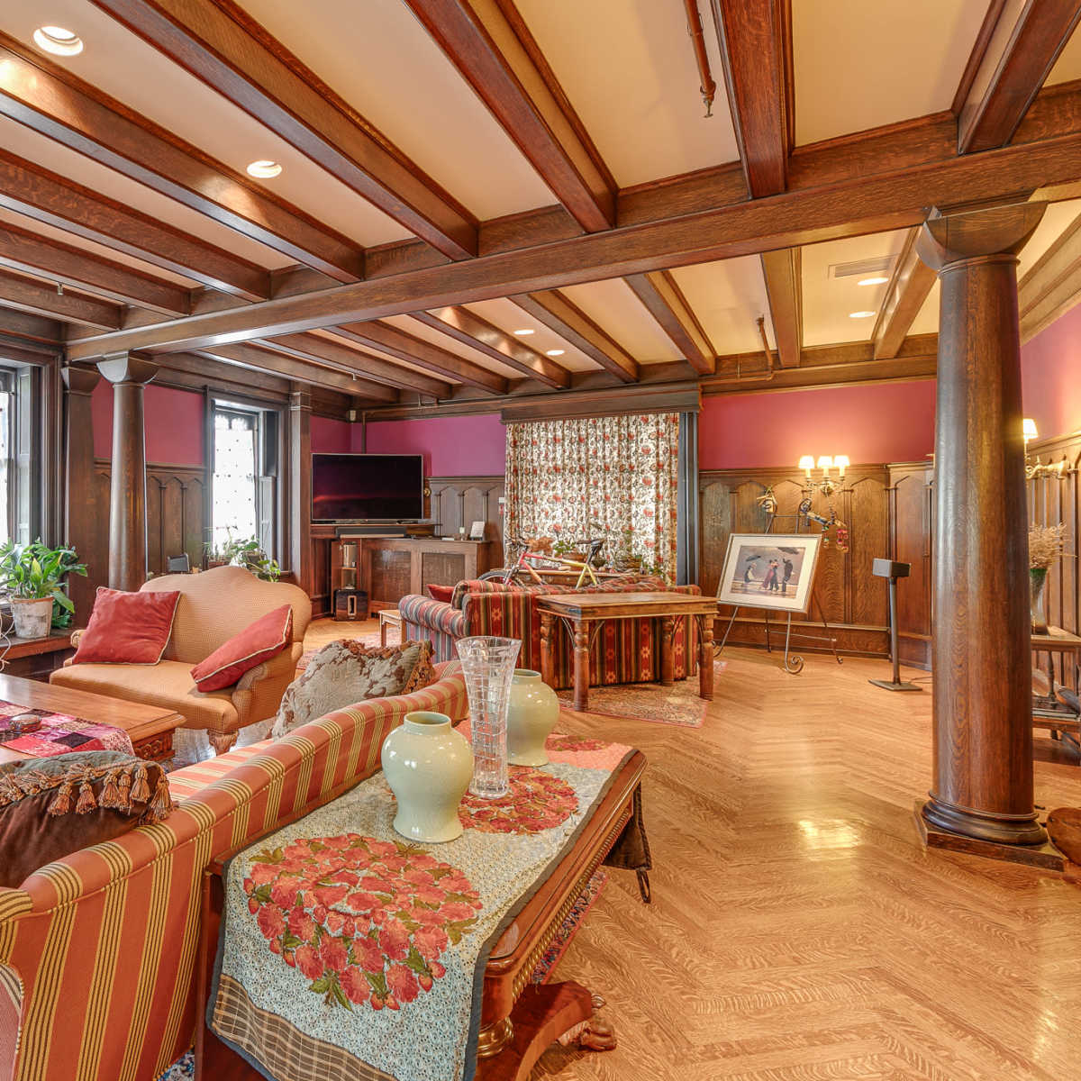 A spacious living room with wooden beam ceilings, a central fireplace, and a combination of seating arrangements around a coffee table.