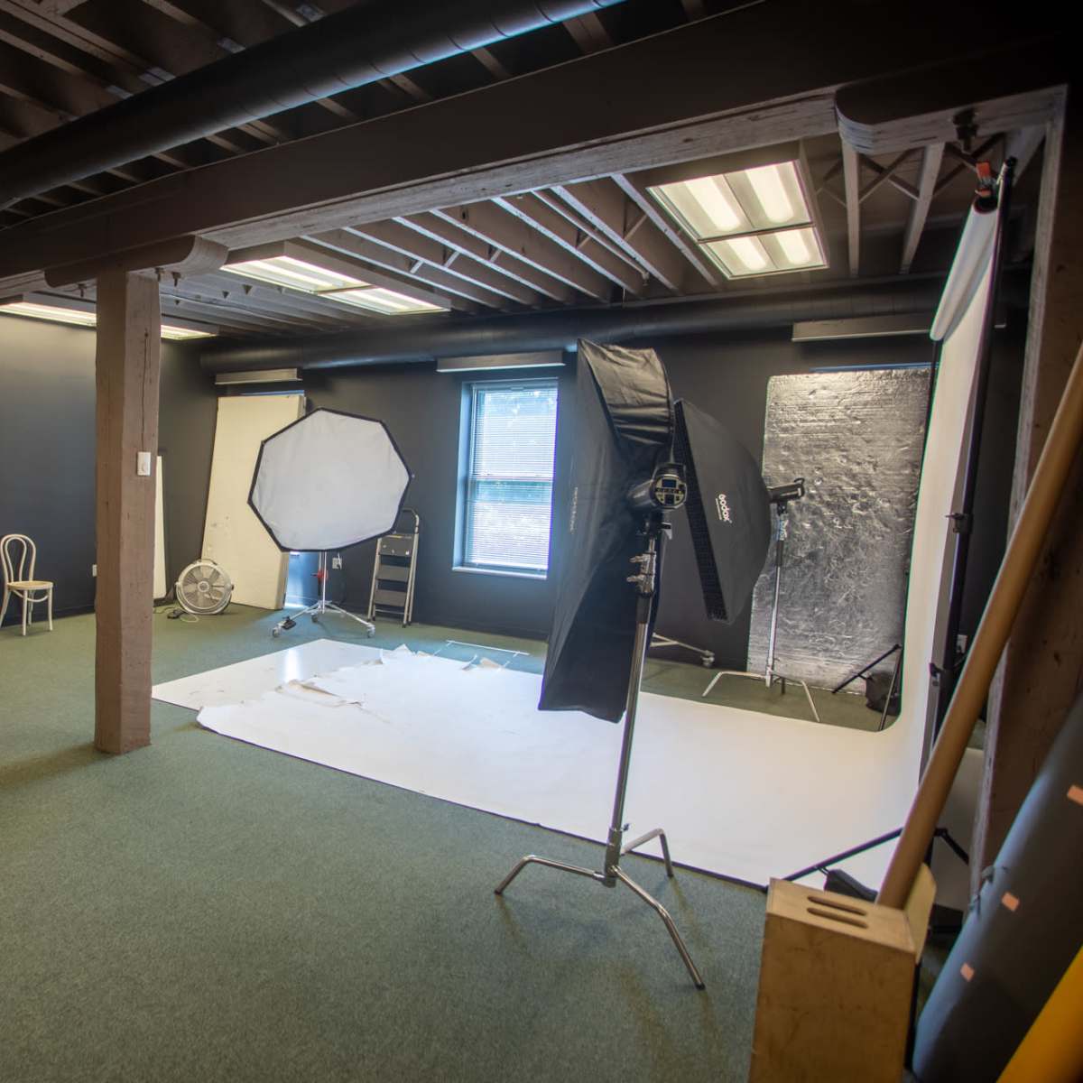 A spacious photography studio with a white backdrop, lighting equipment, and seating arrangements against dark walls.