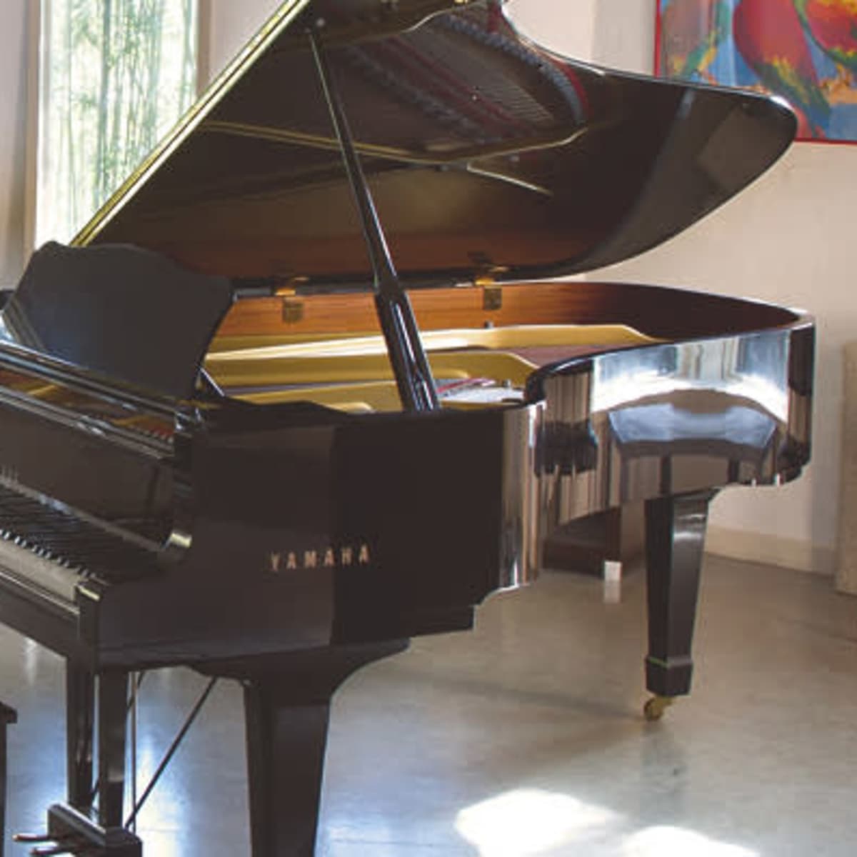 A black Yamaha grand piano is positioned in a well-lit room with large windows and minimalist decor.