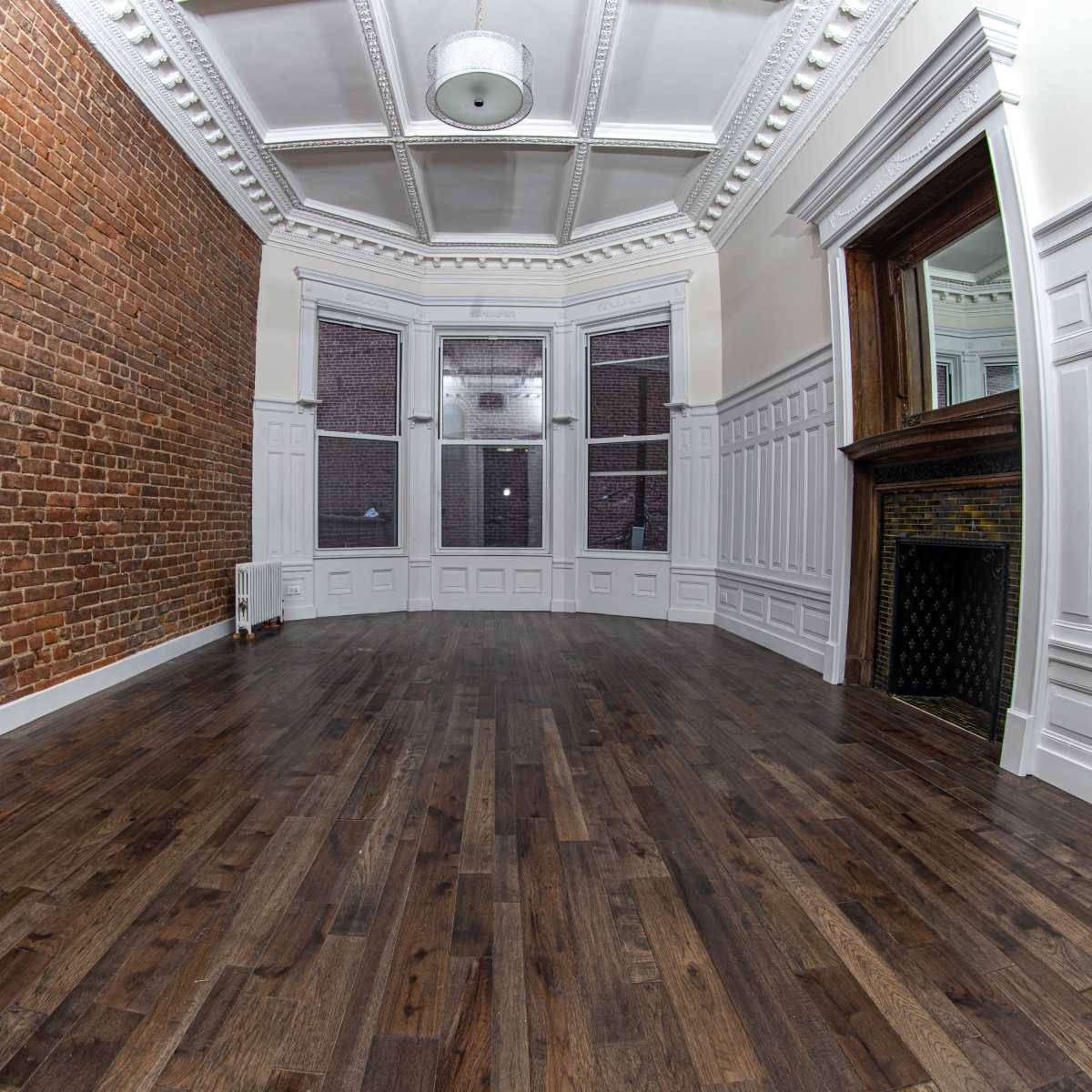 A spacious, empty room with a brick wall on one side, wooden flooring, and a decorative ceiling.
