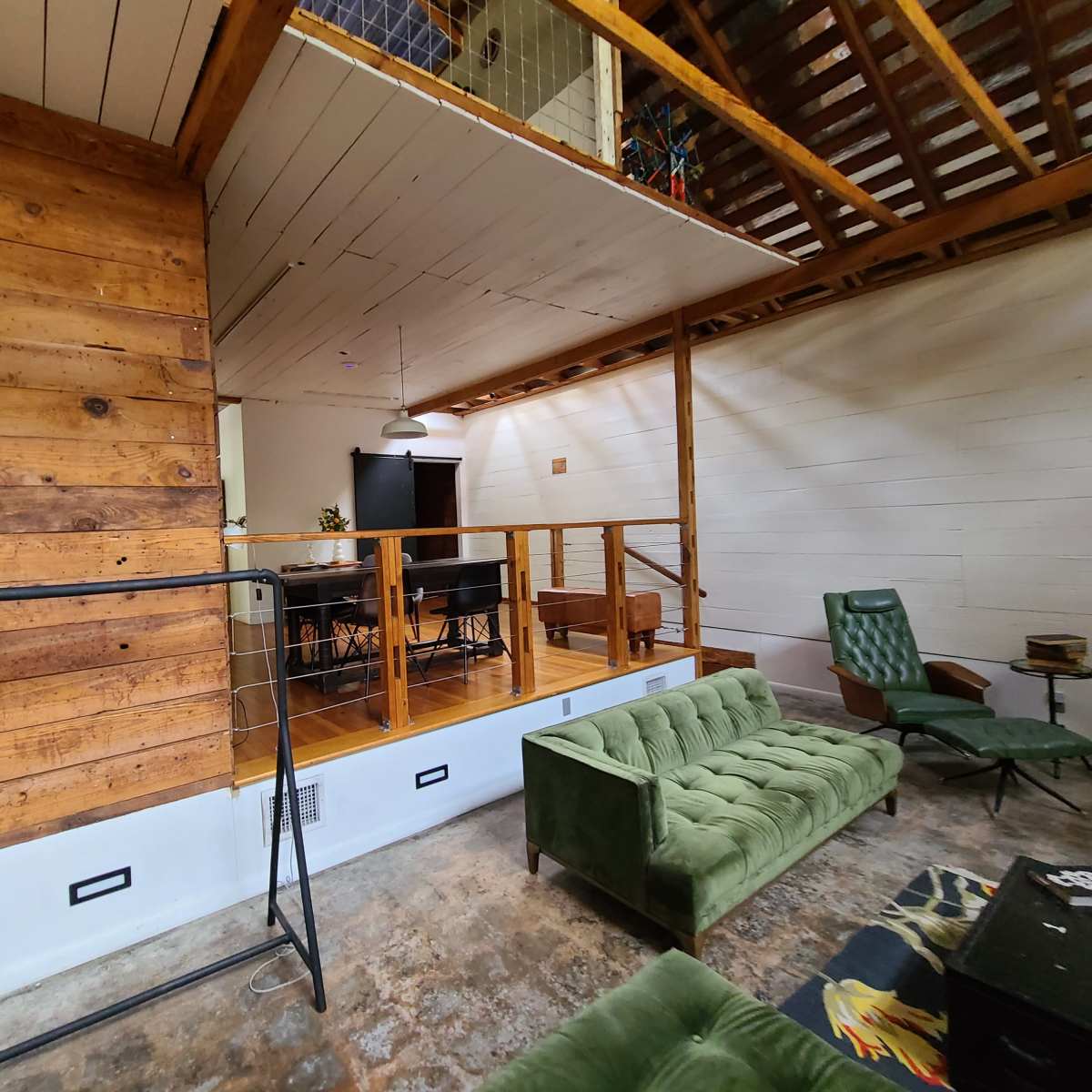 A living space with wooden walls, a green sofa, and a dining area featuring a table and chairs on an elevated platform.